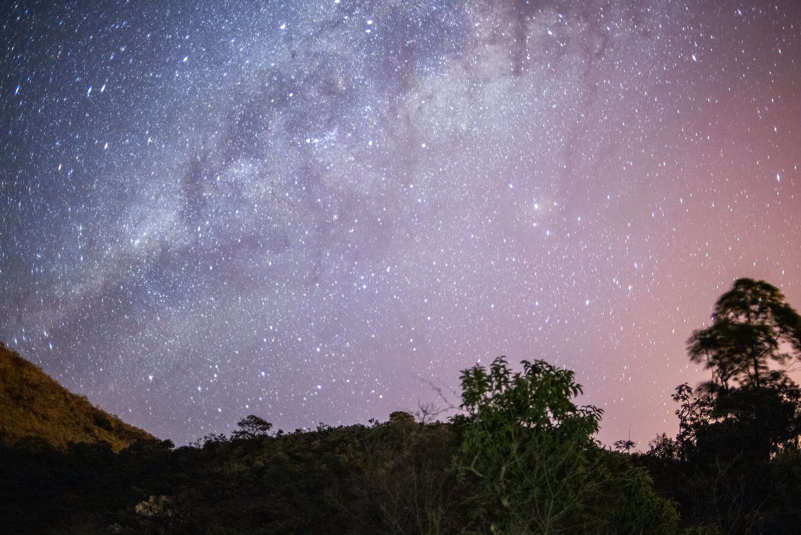 Arco da Via Láctea sobre um vale com árvores