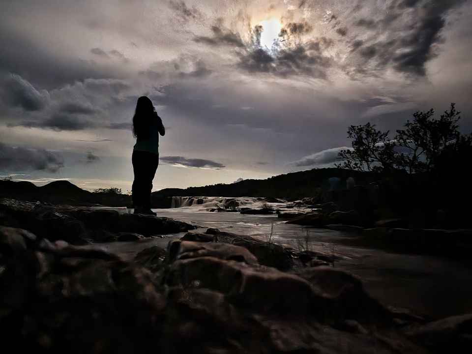 Pessoa em silhueta, de costas, contemplando a lua sobre o rio
